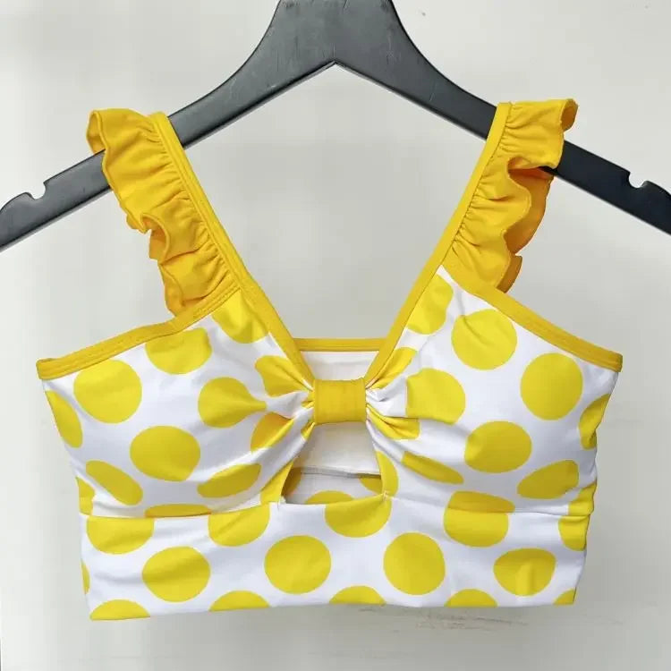 Yellow and white polka dot bikini top on a hanger against a white background