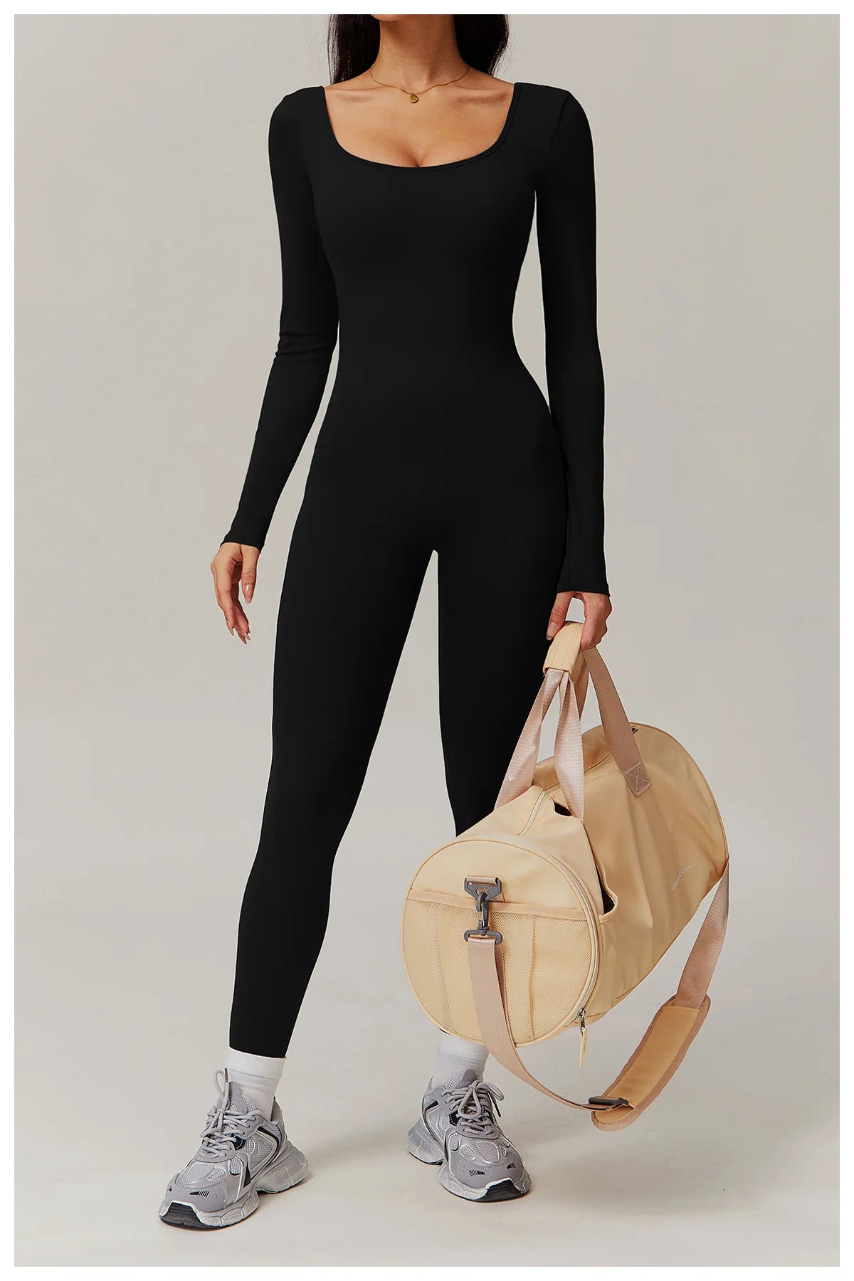Person wearing a black outfit holding a beige duffel bag on a plain background
