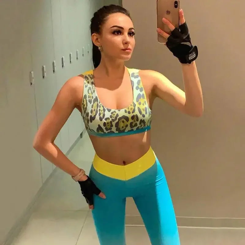 Woman taking a mirror selfie wearing a leopard print sports bra and blue leggings.